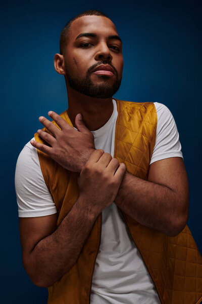 Африканский американец в желтом жилете слегка улыбается на темно-синем фоне, концепция моды