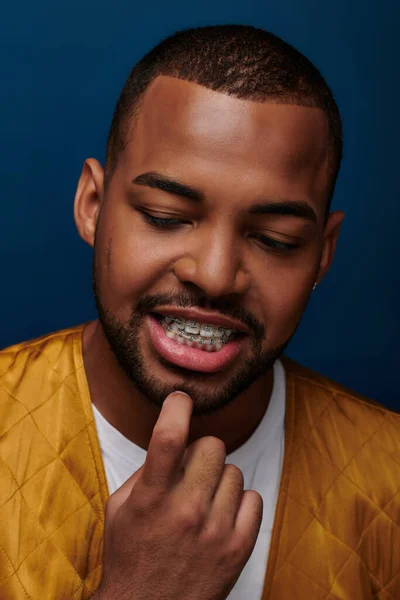 stock image smiley african american male model with braces looking down with finger on chin, fashion concept