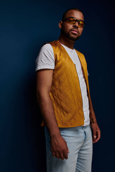 молодой стильный мужчина в желтом жилете и солнцезащитных очках, стоящий неподвижно глядя на камеру, концепция моды