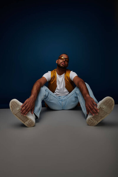 красивый мужчина в стильной повседневной одежде позируя на полу с руками к ногам, концепция моды