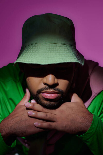 close up young bearded man in green sweatshirt and panama putting his head on hands, fashion concept