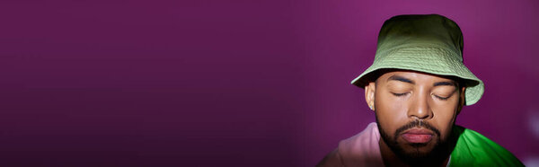бородатый молодой человек в зеленой Панаме с бриллиантовой серьгой и закрытыми глазами, концепция моды, баннер