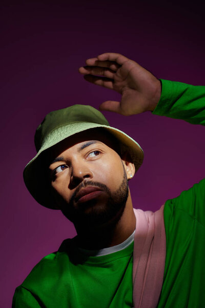 молодой стильный мужчина с сережкой и слегка поднятой рукой на фиолетовом фоне, концепция моды