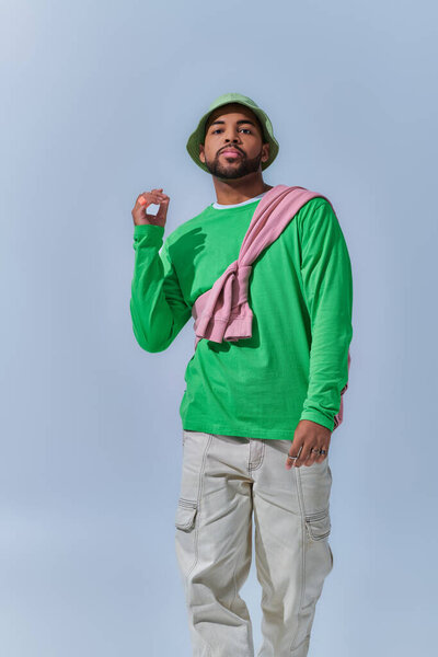 Африканский американец с поднятой рукой смотрит на камеру на голубом фоне, концепция моды