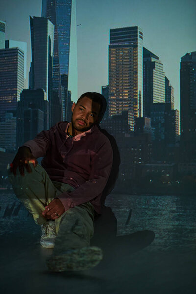 красивый молодой человек в уличной одежде сидит на полу в цифровом проекторе огней, концепция моды