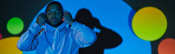 young man putting on hood with closed eyes in digital projector lights, fashion concept, banner