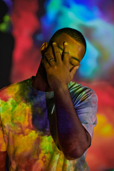 красивый мужчина в уличной одежде закрывает лицо рукой в цифровых проекторах, концепция моды