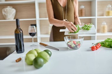 Modern mutfaktaki taze malzemelerden salata yapan, kıvırcık salata kesen bir kadın.