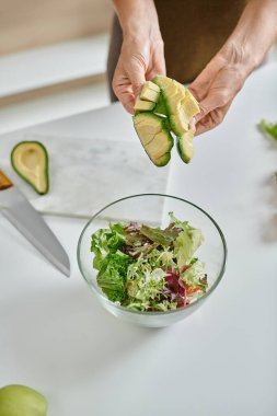 close up of cropped woman holding sliced ripe avocado near lettuce in bowl and glass of red wine clipart