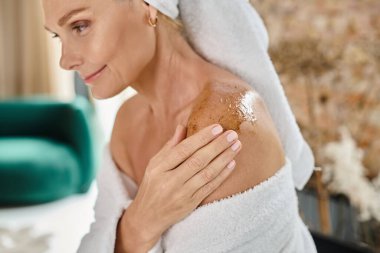 beautiful middle aged woman with white towel on head and bathrobe using body scrub on shoulder clipart