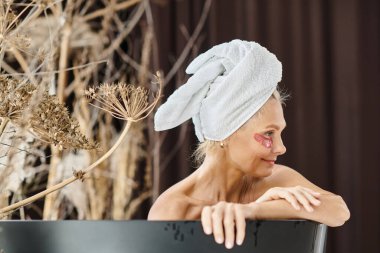 Kafasında beyaz havluyla ve göz bantlarının altında banyo yapan orta yaşlı güzel bir kadın.