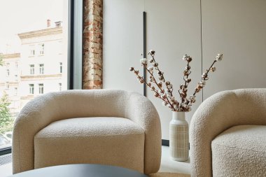 Vazoda, modern oturma odasında, pamuk dallarının yanında iki rahat ve beyaz koltuk.