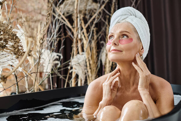 relaxed middle aged woman with white towel on head and under eye patches taking bath at home