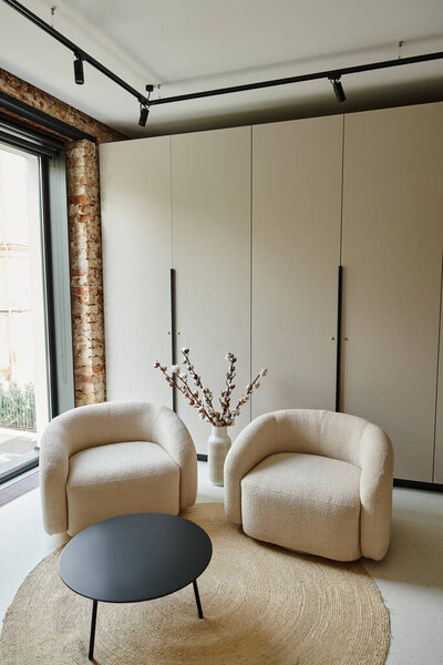 two comfortable armchairs next to black coffee table and cotton branches in vase, modern living room