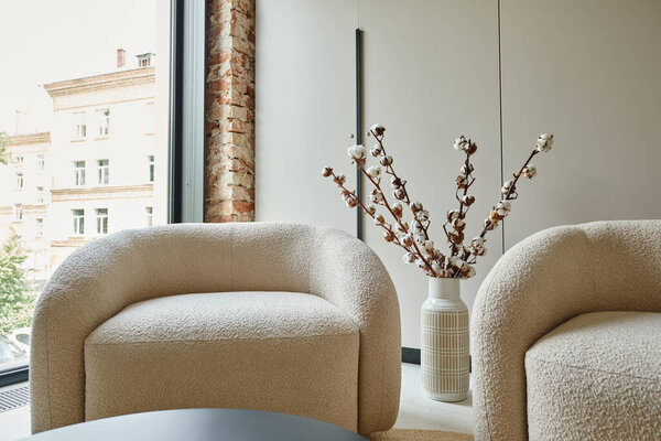 two comfortable and white armchairs next to cotton branches in vase, modern living room