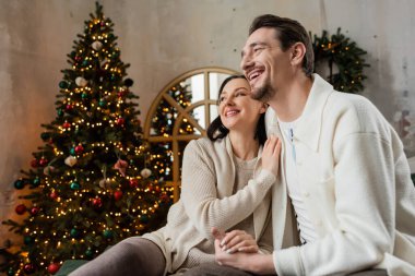 Neşeli evli çift, karı koca, bulanık Noel ağacının yanında oturuyor, neşe mevsimi.