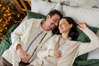 Mutlu evli çiftin mutlu sabahlarını bulanık Noel ağacının yanında yatakta geçirmesinin üst görüntüsü.