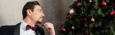 well-dressed gentleman with beard wearing tuxedo with bow tie looking at Christmas tree, banner clipart