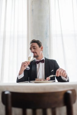 Smokinli iyi giyimli bir beyefendi biftek yerken şampanyanın tadını çıkarıyor, zengin bir hayat.