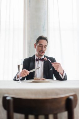 Smokinli iyi giyimli bir beyefendi şampanya bardağının yanında lezzetli biftek yiyor, zengin bir hayat.