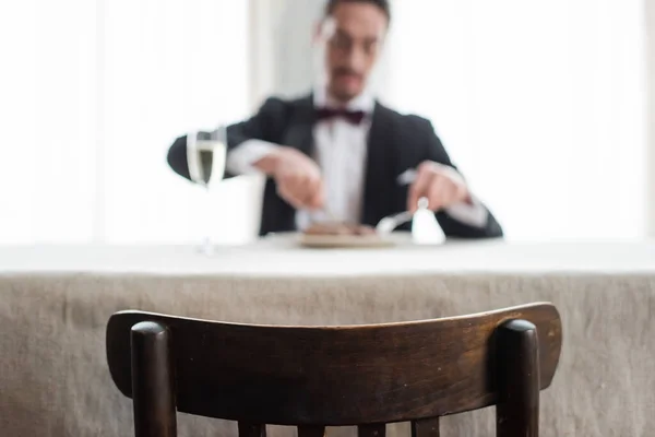 stock image focus on wooden chair, wealthy gentleman in tuxedo enjoying dinner at home, natural light