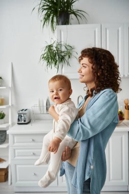 Romper 'daki neşeli çocuk evde annesinin elinde kameraya bakıyor, mutlu bir çocukluk.