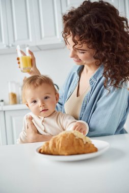 Lezzetli kruvasana bakan tatlı bir bebek. Yanında da bir bardak portakal suyu ve lezzetli bir kahvaltı.