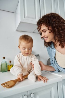 Küçük kızının yanında ahşap çatallı neşeli bir kadın mutfak atölyesinde oturuyor, mutlu sabahlar.