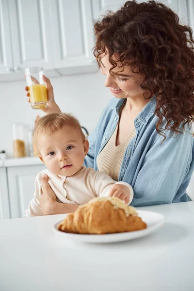 Lezzetli kruvasana bakan tatlı bir bebek. Yanında da bir bardak portakal suyu ve lezzetli bir kahvaltı.