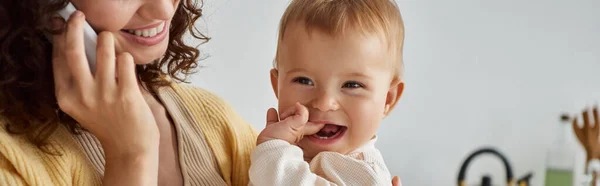 stock image smiling mother talking on smartphone near little carefree daughter at home, happy parenting, banner