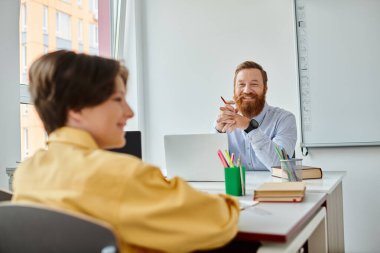 A man sits attentively at a desk, engaged in conversation with a child. clipart