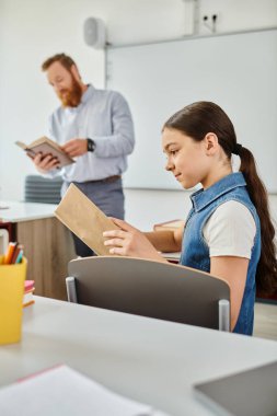 Masaya oturmuş, kitap okumaya dalmış bir kız..