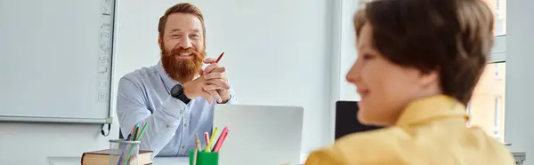 stock image A man sits at a desk, teaching, while a young boy in front of him listens intently.