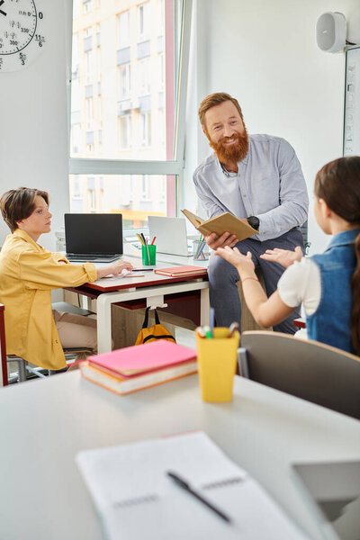 A group of people sit around a table in a bright, lively classroom, as a male teacher instructs them on various topics and engages in interactive discussions.