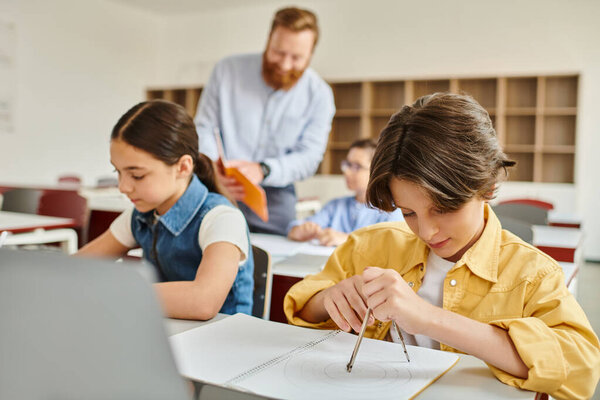 A group of children sit attentively at desks while a male teacher instructs them in a bright, lively classroom.