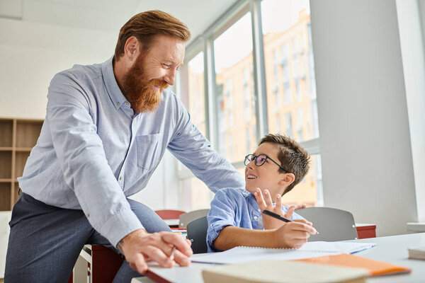 A teacher assists a young boy with his homework in a vibrant and engaging classroom setting