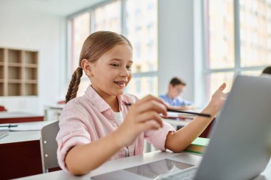 Odaklanmış ifadesi olan genç bir kız bir dizüstü bilgisayarın önünde oturuyor, çevrimiçi öğrenim ya da eğitim faaliyetleriyle ilgileniyor.