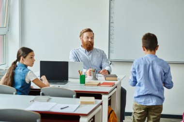 Bir adam bir grup çocuğun önünde masada oturuyor, onları canlı bir sınıfa yerleştiriyor..