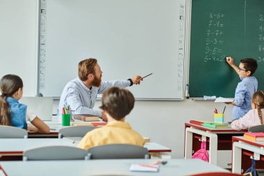 Bir erkek öğretmen, bir grup öğrenciyle parlak ve canlı bir sınıf ortamında, öğrenme ve yaratıcılıkla dolu.