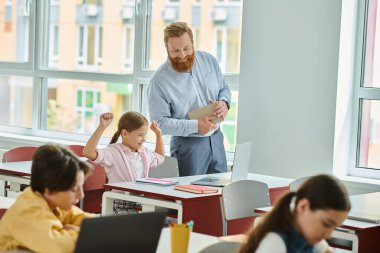 Tutkulu bir erkek öğretmen, canlı bir sınıf ortamında çeşitli nişanlı öğrencilerden oluşan bir grubun önünde büyüleyici bir ders veriyor..