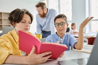 Büyüleyici bir ifadeye sahip bir çocuk, bir arkadaşına kitap okur, dikkatle dinler, yüzleri yumuşak ışıkla aydınlanır..