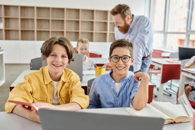 Bir çift çocuk, parlak, canlı bir sınıf ortamında öğretmenlerinin rehberliğinde bir dizüstü bilgisayarla uğraşıp keşfediyor ve öğreniyorlar..