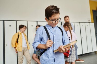 A young boy in a blue shirt and suspenders is engrossed in a book he is holding in his hands, captivated by the words on its pages. clipart