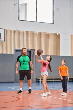 Basketbol teknikleri gösteren bir adam, çocuklarla enerji ve heyecan dolu bir spor salonunda oynuyor..