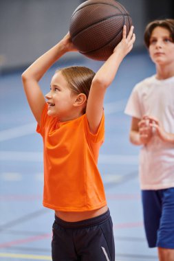 Genç bir kız sevinçle basketbol topunu havaya kaldırıyor, oyun için heyecan ve tutku hissi yayıyor..
