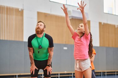Bir adam ve genç bir kız enerjik bir şekilde spor salonunda basketbol oynuyorlar, takım çalışması, yetenek ve dostluk sergiliyorlar..