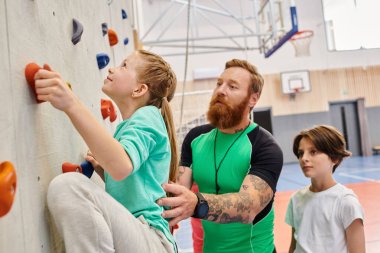 Öğretmen gibi davranan bir adam, parlak ve canlı bir sınıfın duvarına tırmanırken iki çocuğa liderlik eder..