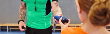 Yeşil tişörtlü bir adam canlı ve enerjik bir spor salonunun ortasında mavi bir ip tutuyor.
