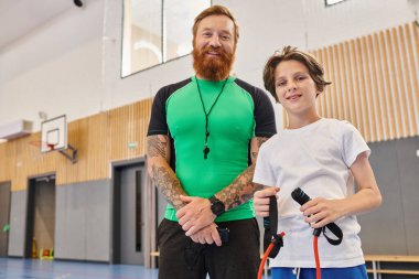 A man stands next to a boy in a gym, engaging in physical activities and fitness training together. clipart