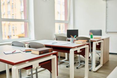 Sınıf boş oturuyor, sıralar ve sandalyeler düzenli sırada dizilmiş.